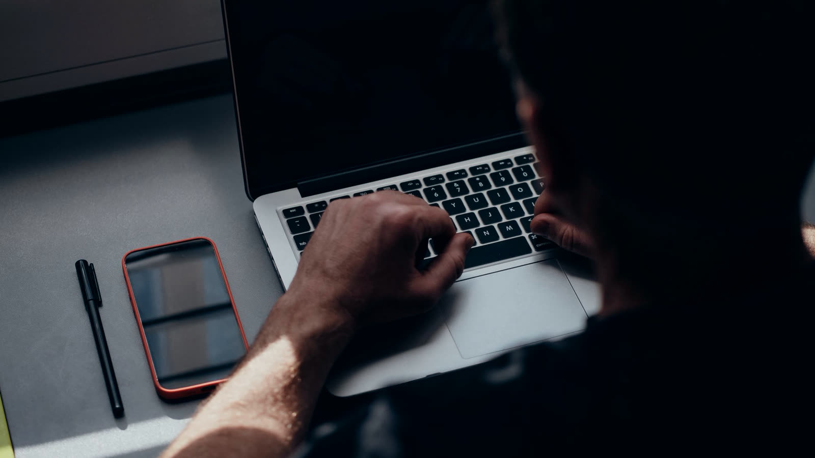 Händer som skriver på en laptop med en mobil bredvid